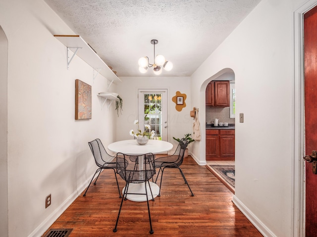 dining area with arched walkways, dark wood-type flooring, a textured ceiling, a chandelier, and baseboards