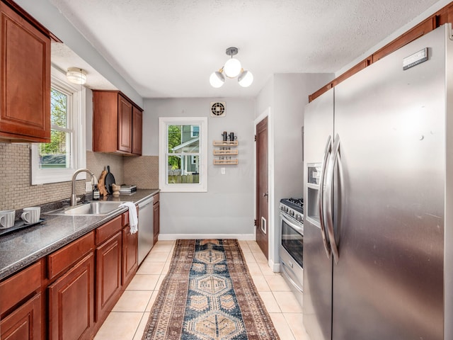 kitchen featuring stainless steel appliances, backsplash, a sink, dark countertops, and plenty of natural light
