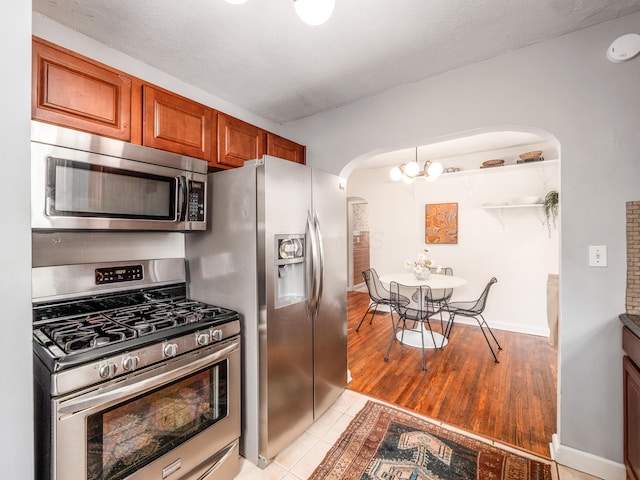 kitchen featuring stainless steel appliances, arched walkways, brown cabinetry, and baseboards