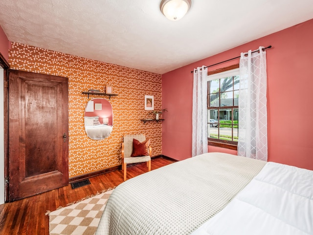 bedroom with baseboards, wood finished floors, and wallpapered walls