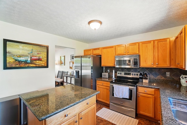8380 Squad Dr, Galloway, OH 43119 - kitchen featuring appliances with stainless steel finishes, decorative backsplash, dark stone countertops, a center island, and a textured ceiling