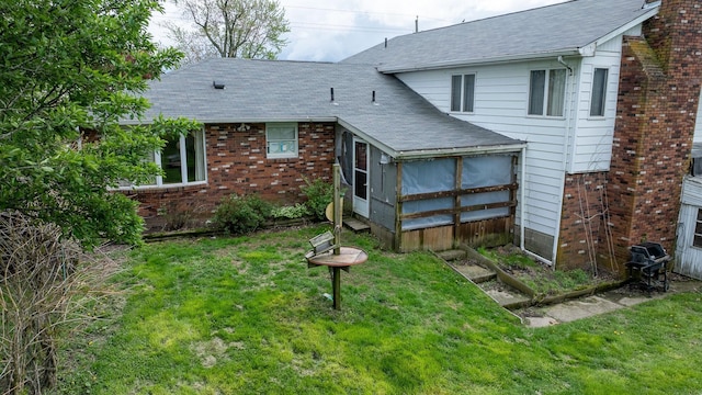 rear view of house featuring a shingled roof, a sunroom, brick siding, and a yard