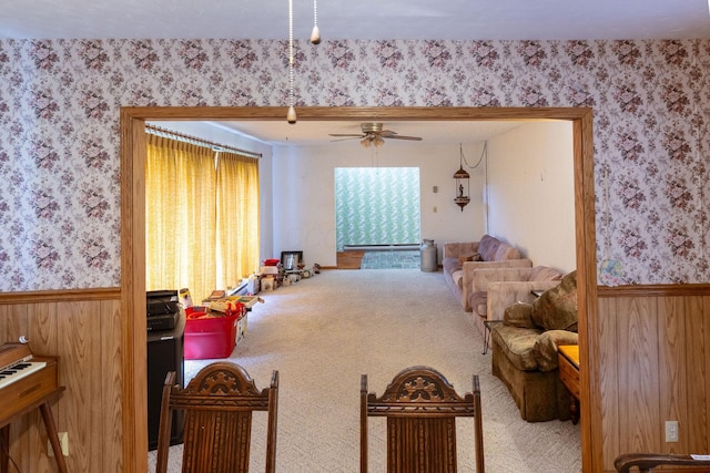 sitting room featuring wallpapered walls, carpet flooring, ceiling fan, and wainscoting