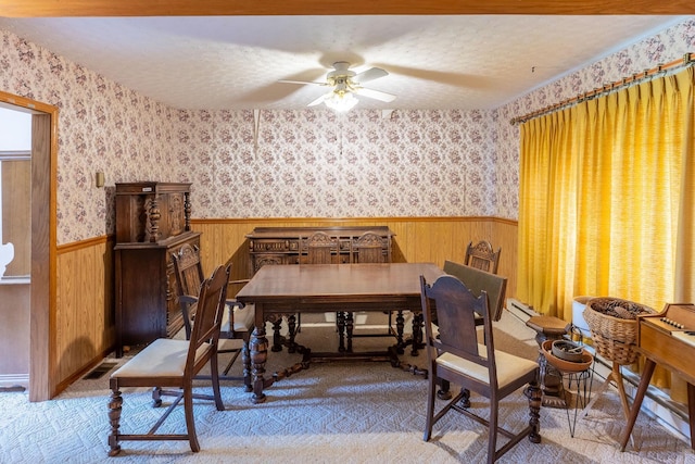 dining space with a ceiling fan, a wainscoted wall, wallpapered walls, and a textured ceiling