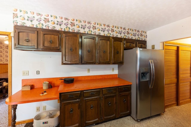 kitchen featuring stainless steel refrigerator with ice dispenser, wallpapered walls, light colored carpet, and dark brown cabinets
