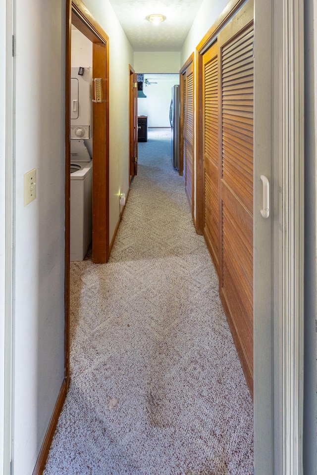 hallway with stacked washer / dryer and carpet flooring