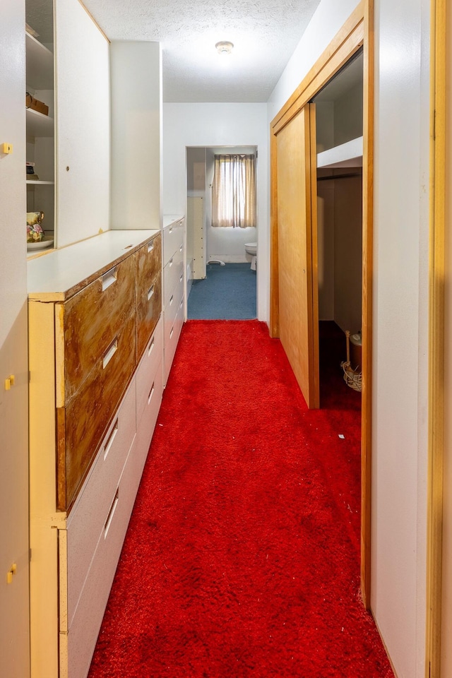 hall with dark colored carpet and a textured ceiling