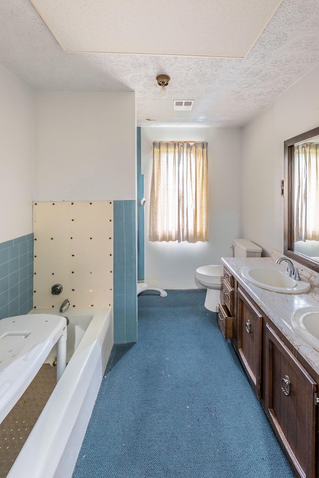 full bathroom featuring plenty of natural light, a bathtub, double vanity, a textured ceiling, and toilet