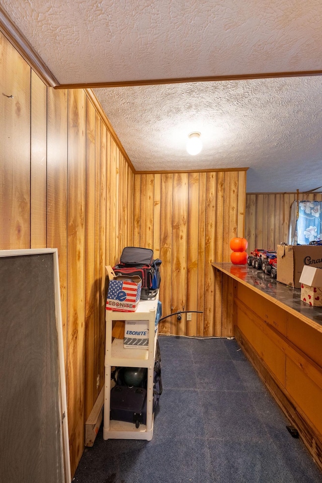 miscellaneous room featuring wooden walls, a textured ceiling, and dark colored carpet