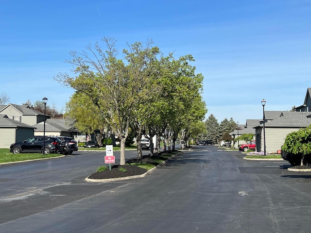 view of asphalt road with a residential view, street lighting, and curbs