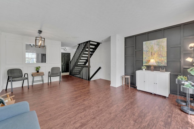 living area with a decorative wall, wood finished floors, stairs, and a chandelier