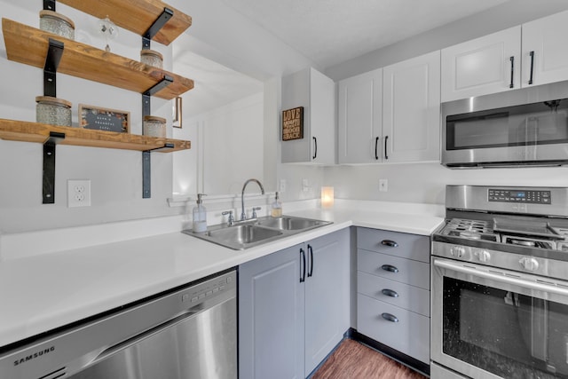 kitchen with stainless steel appliances, open shelves, a sink, and light countertops