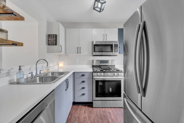 kitchen with stainless steel appliances, a sink, dark wood-style flooring, light countertops, and white cabinetry