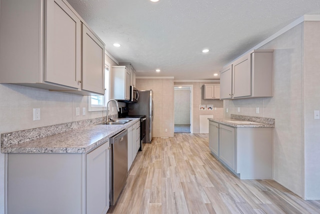 kitchen featuring stainless steel appliances, a sink, light wood-style floors, light countertops, and a textured ceiling
