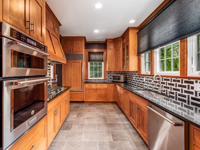 10 Park Dr, Columbus, OH 43209 - kitchen with stainless steel appliances, a sink, dark stone counters, brown cabinetry, and decorative backsplash