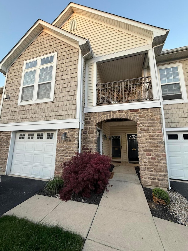 view of front of property featuring a balcony, stone siding, a garage, and asphalt driveway