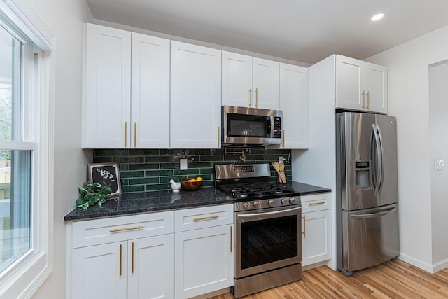 549 Hanford St, Columbus, OH 43206 - kitchen featuring appliances with stainless steel finishes, tasteful backsplash, white cabinets, light wood-style flooring, and dark stone counters
