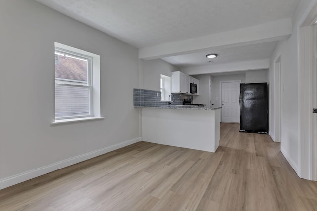 kitchen featuring black appliances, a peninsula, light wood-style floors, plenty of natural light, and beam ceiling