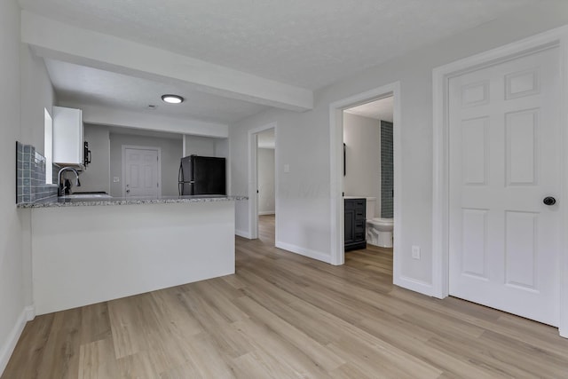 kitchen featuring black appliances, a sink, light wood finished floors, baseboards, and a textured ceiling
