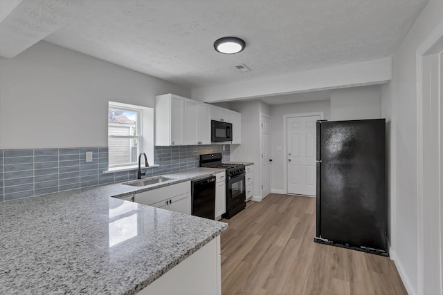 kitchen featuring black appliances, a sink, a textured ceiling, light wood finished floors, and backsplash