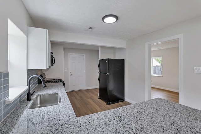 kitchen with black appliances, a sink, wood finished floors, decorative backsplash, and white cabinetry