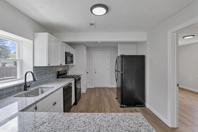 kitchen featuring black appliances, a sink, wood finished floors, white cabinets, and decorative backsplash