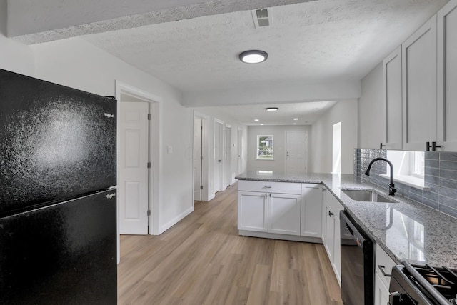 kitchen with black appliances, a sink, light wood finished floors, a peninsula, and backsplash