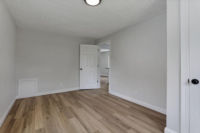 unfurnished room featuring light wood-type flooring, baseboards, and a textured ceiling