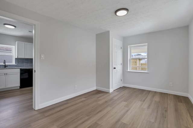 unfurnished room featuring light wood-type flooring, a sink, baseboards, and a textured ceiling