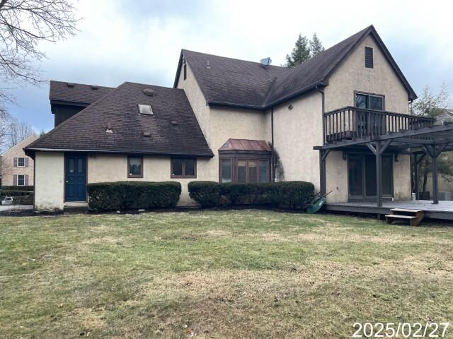 back of property featuring stucco siding, a wooden deck, a yard, and a balcony