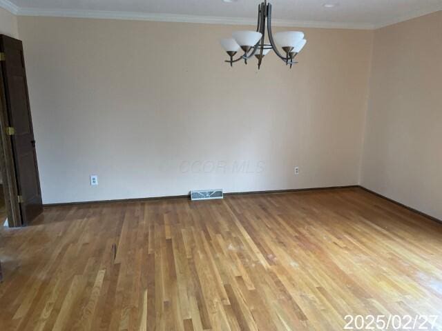spare room with a chandelier, light wood-style flooring, crown molding, and baseboards