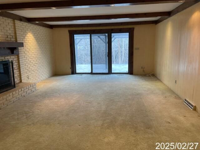 unfurnished living room featuring beam ceiling, light carpet, and a brick fireplace