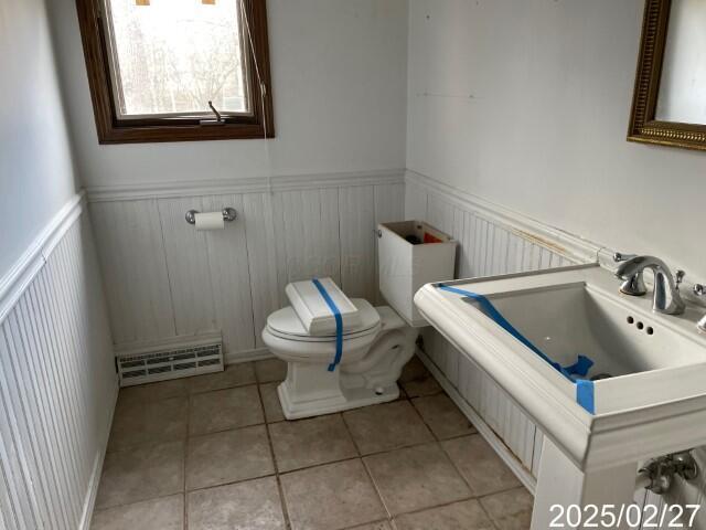 half bath with toilet, wainscoting, and tile patterned flooring