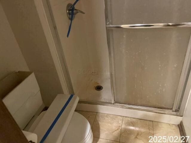 bathroom with a shower stall, toilet, and tile patterned floors