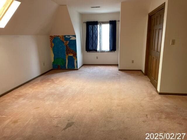 unfurnished bedroom featuring light colored carpet, vaulted ceiling, baseboards, and a skylight