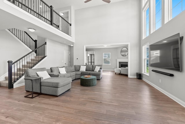 living area with a high ceiling, ceiling fan, wood finished floors, stairs, and baseboards