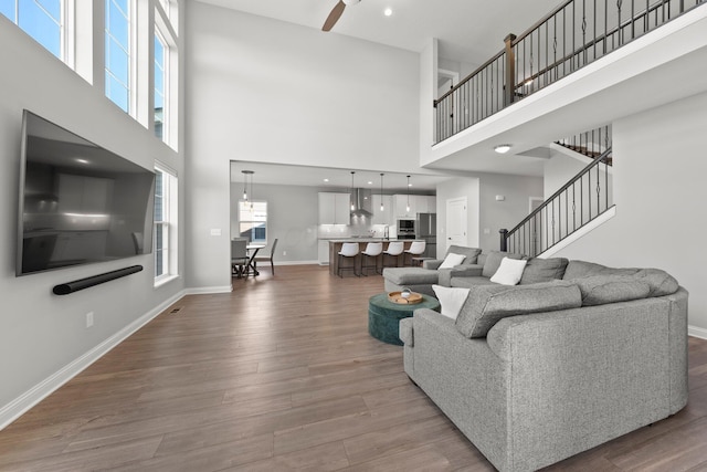 living room featuring a towering ceiling, wood finished floors, baseboards, and a ceiling fan