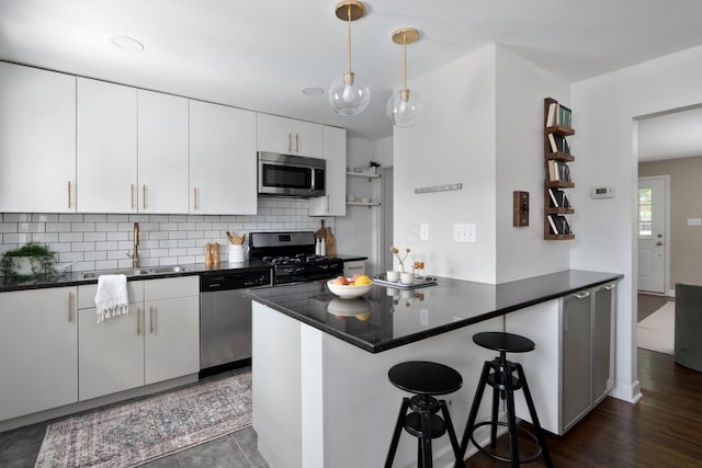 1809 NW Ct Unit E, Columbus, OH 43212 - kitchen featuring appliances with stainless steel finishes, dark countertops, a peninsula, backsplash, and a kitchen bar