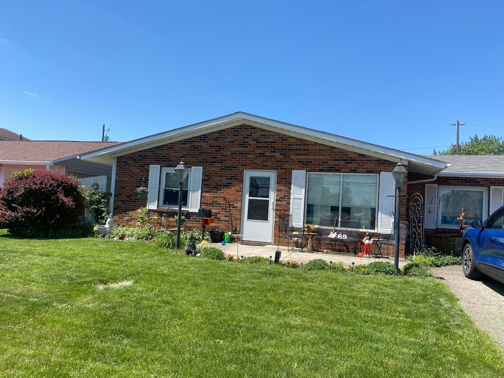 ranch-style home with brick siding, a front lawn, and a patio