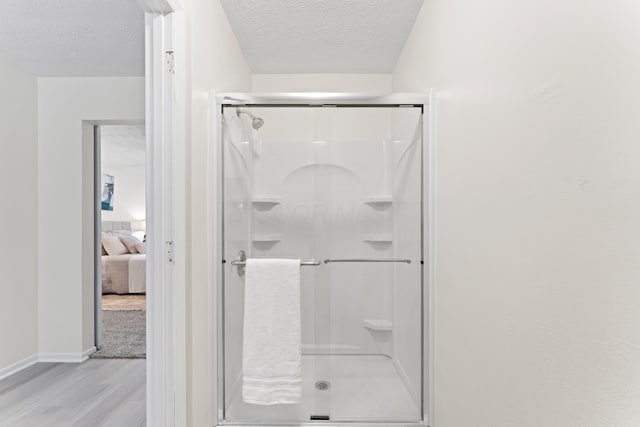 full bath featuring a textured ceiling, wood finished floors, a stall shower, ensuite bathroom, and baseboards