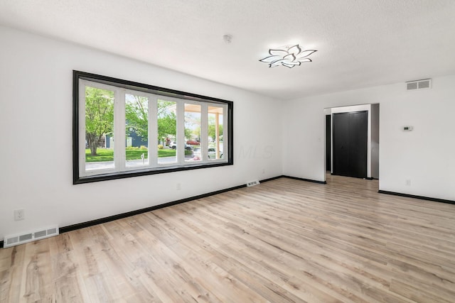 spare room with light wood finished floors, baseboards, and a textured ceiling