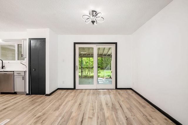 unfurnished dining area with light wood-style floors, baseboards, a textured ceiling, and a sink