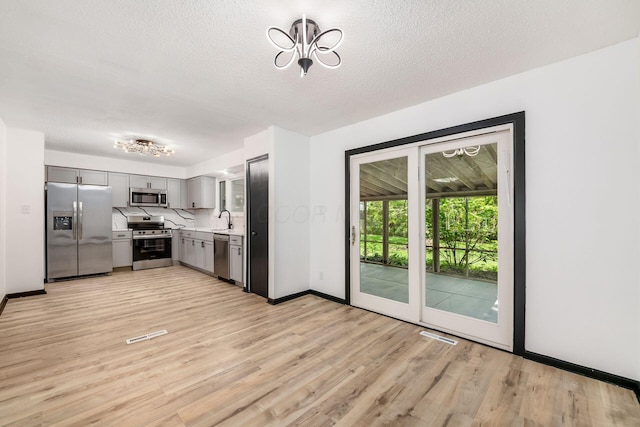 kitchen with appliances with stainless steel finishes, gray cabinets, light countertops, light wood finished floors, and a textured ceiling