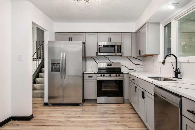 kitchen with stainless steel appliances, gray cabinets, a sink, light wood finished floors, and a textured ceiling