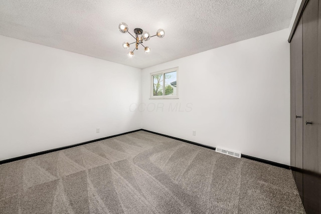 unfurnished room featuring a chandelier, carpet flooring, baseboards, and a textured ceiling
