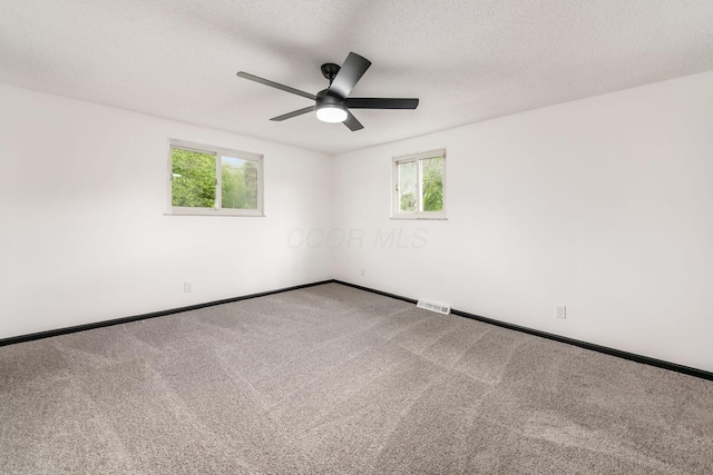 carpeted spare room featuring healthy amount of natural light, ceiling fan, baseboards, and a textured ceiling