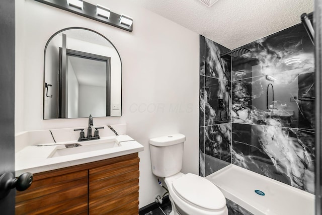 bathroom with toilet, a shower stall, vanity, and a textured ceiling