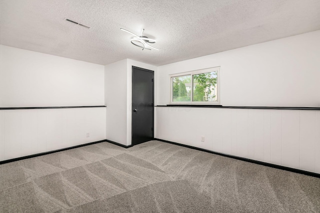 empty room with carpet floors, a textured ceiling, baseboards, and a wainscoted wall