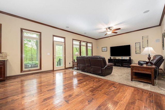 living room with wood-type flooring, healthy amount of natural light, a ceiling fan, crown molding, and baseboards
