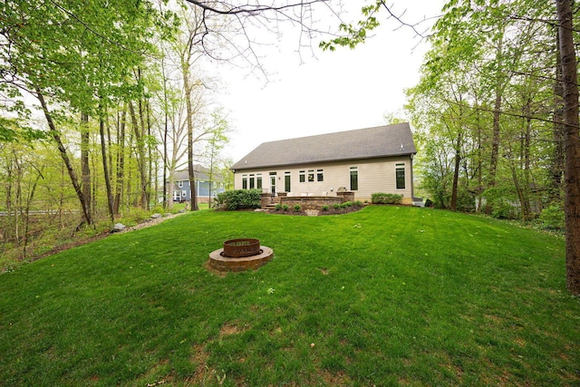 back of house with an outdoor fire pit and a lawn